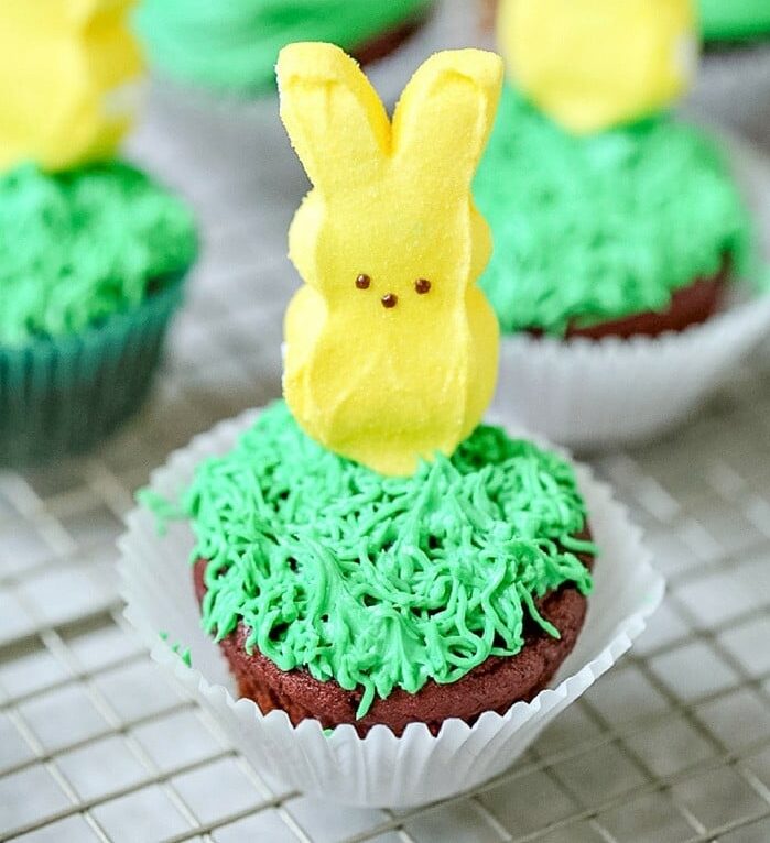 Green frosted cupcakes with yellow marshmallow bunny peeps on top.