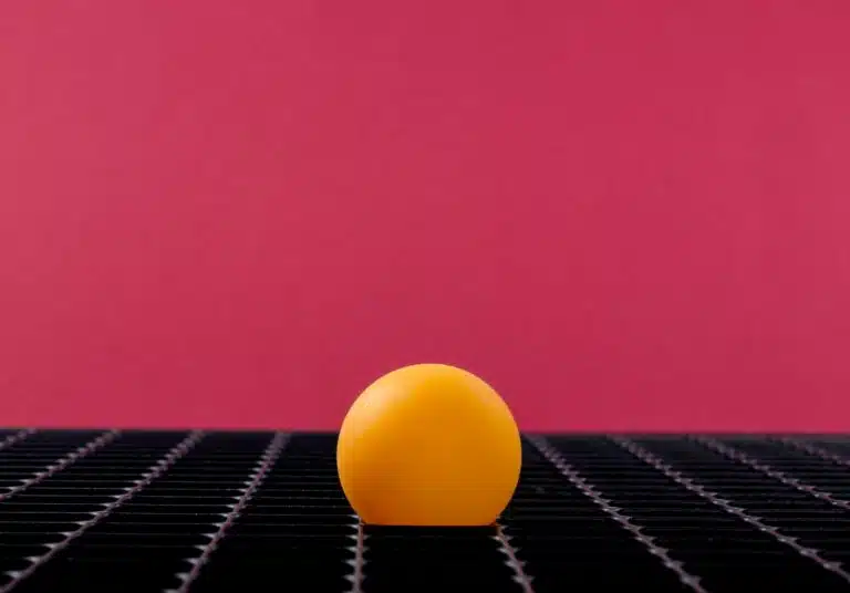 Yellow sphere on black surface in front of a magenta background.